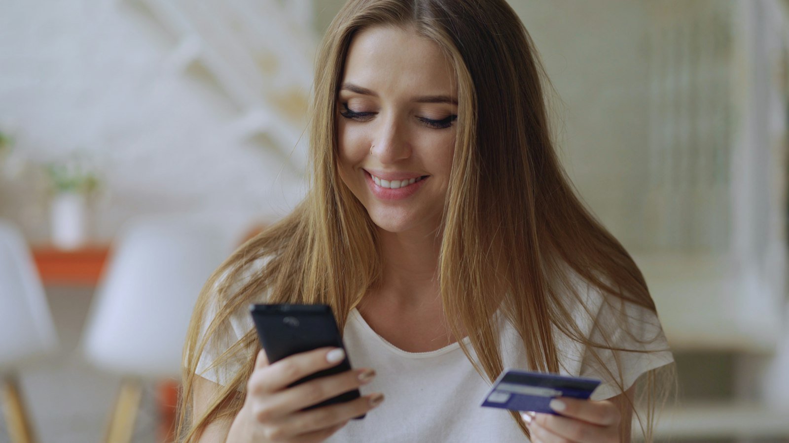 فتاة مبتسمة تمسك هاتفاً وبطاقة دفع